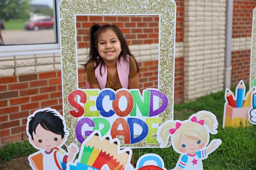A student smiles behind a back-to-school sign
